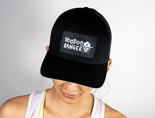 Female model wearing the hat. The front of the hat has a patch that says Voodoo Ranger and has an image of the Voodoo Ranger character's head.