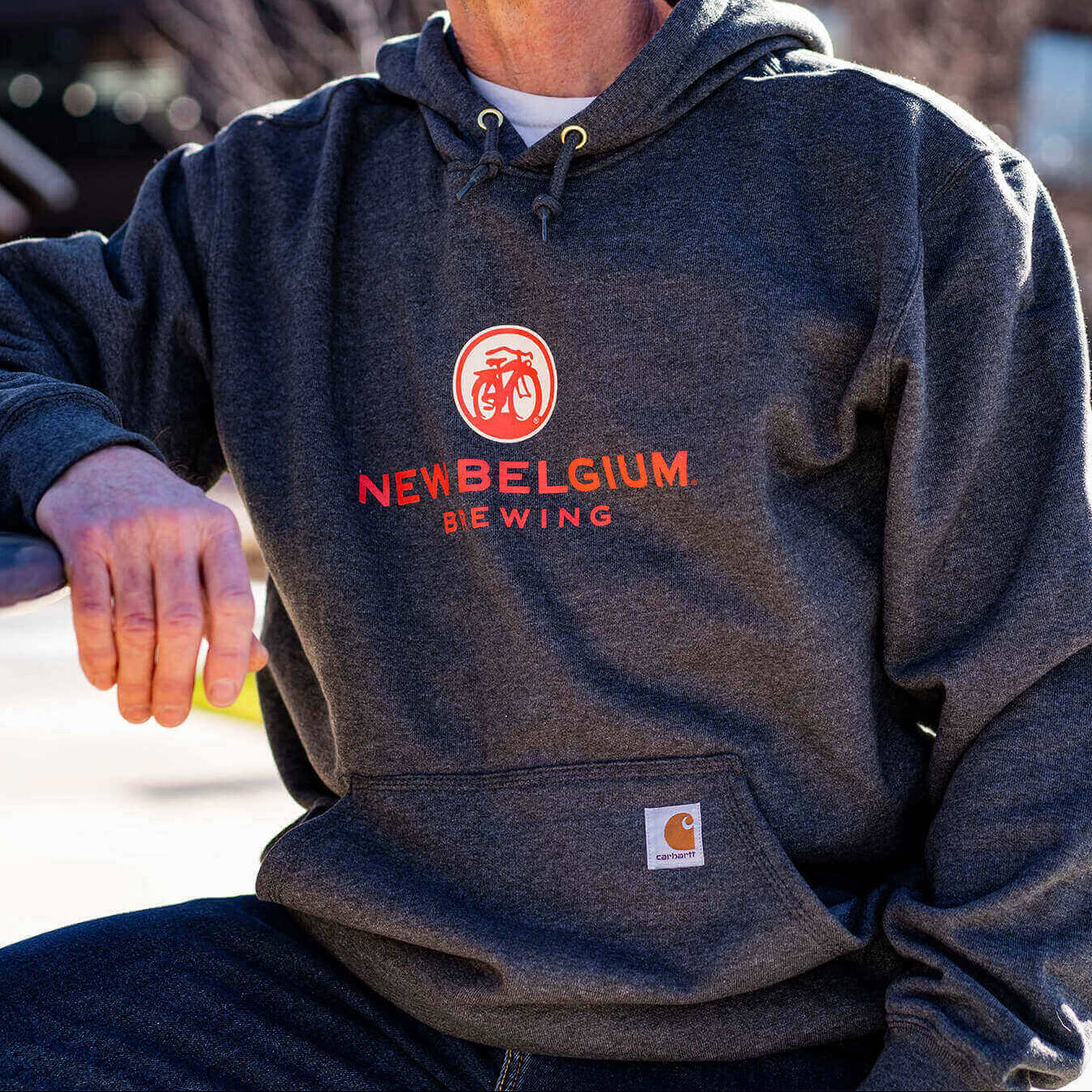 Man wearing heathered gray New Belgium x Carhartt hooded sweatshirt